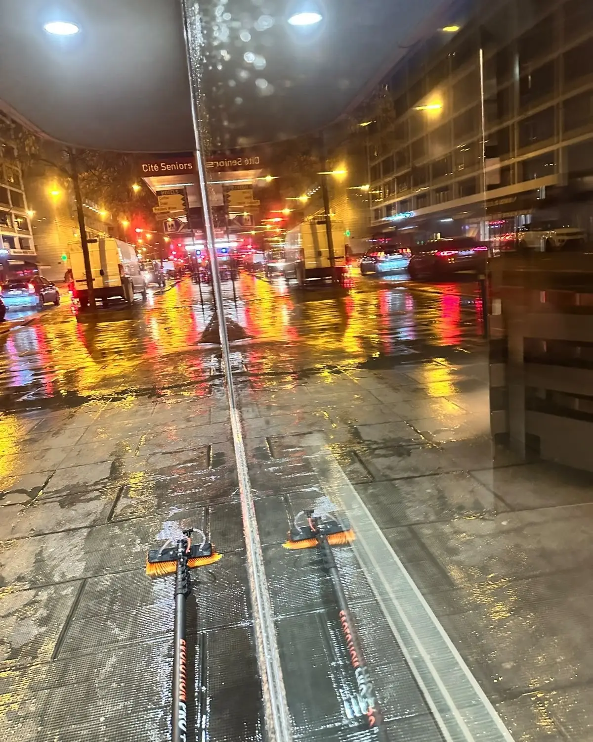 Deux brosses à eau pure reflétées dans une façade vitrée, de nuit